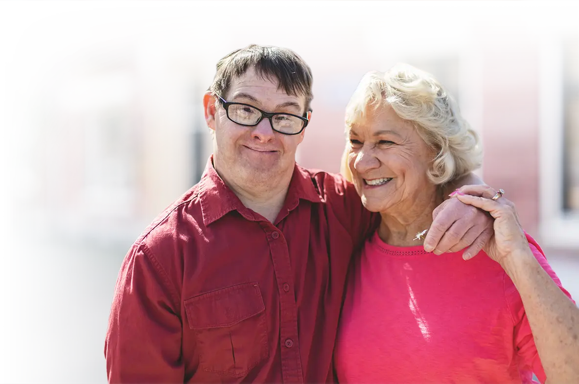 Photo of a man with a developmental disability in a friendly embrace with an older woman.